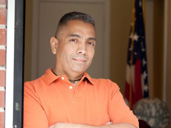 Smiling man in orange polo with his arms crossed