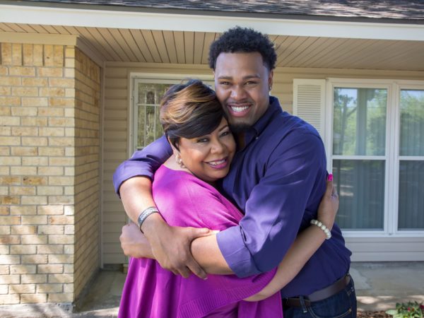 A son and mother hugging outside of a house