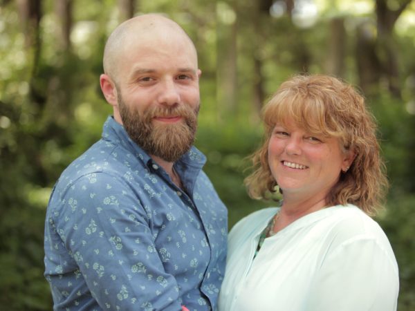 Man and woman smiling with trees in background