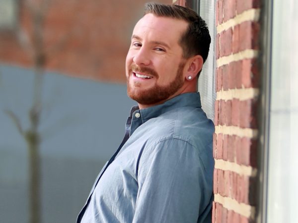 Man smiling and leaning against brick wall