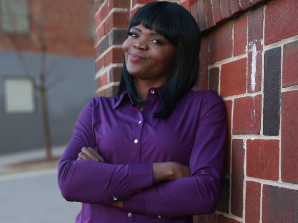 Woman smiling against brick wall with arms crossed