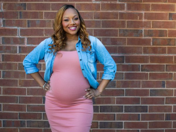 Pregnant woman smiling and holding her stomach in front of brick wall