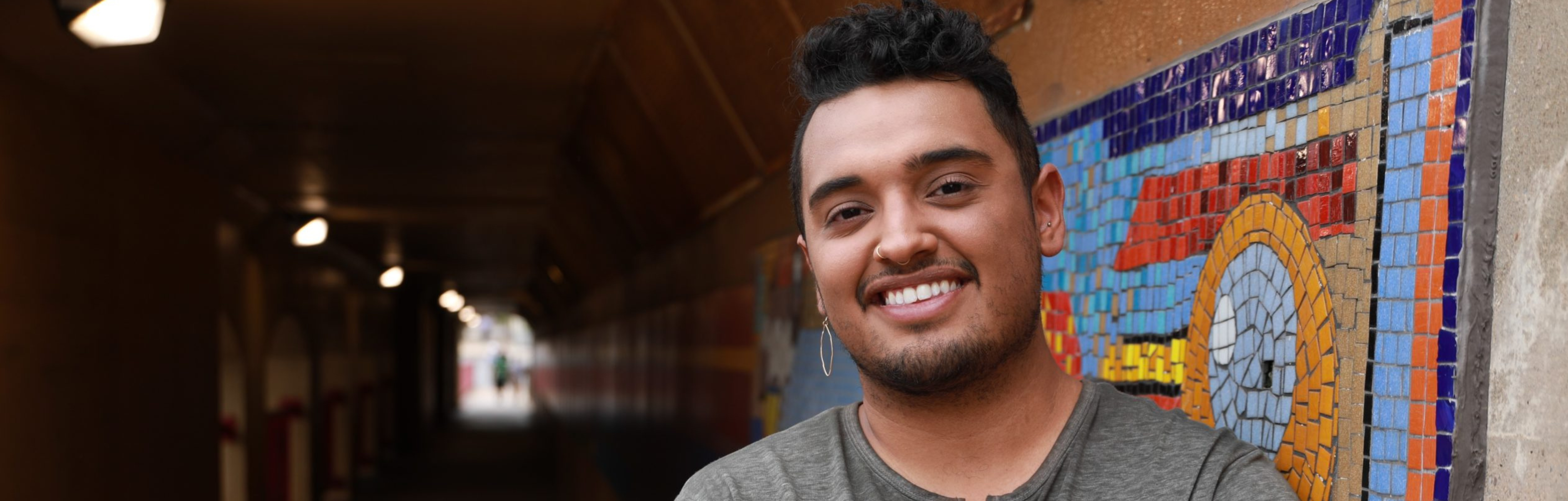 Latinx man smiling and standing against a mosaic wall